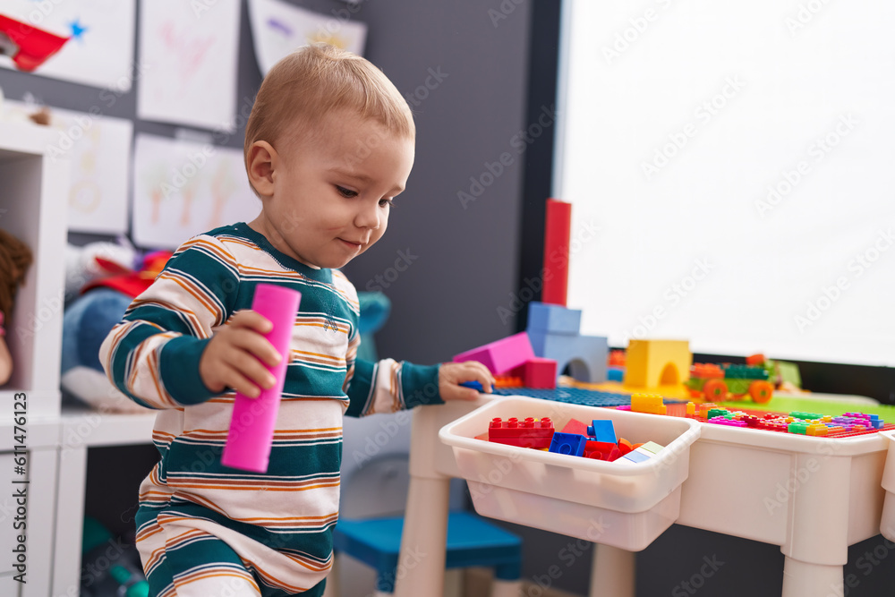 Adorable caucasian baby playing with construction blocks standing at kindergarten