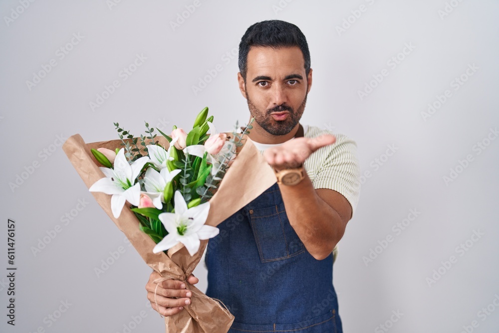 Hispanic man with beard working as florist looking at the camera blowing a kiss with hand on air being lovely and sexy. love expression. Hispanic man with beard working as florist looking at the camera blowing a kiss with hand on air being lovely and sexy. love expression.