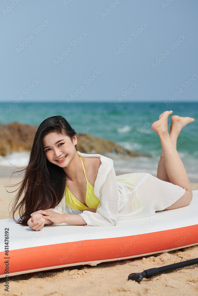 Smiling young woman lying on paddleboard after swimming in sea
