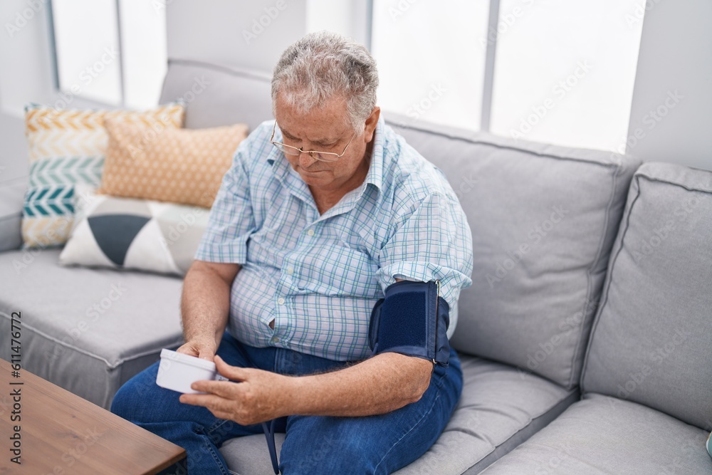Middle age grey-haired man measuring pulse using tensiometer at home Middle age grey-haired man measuring pulse using tensiometer at home