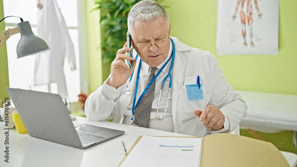 Middle age grey-haired man doctor talking on smartphone reading medical report at clinic