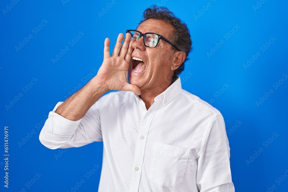 Middle age hispanic man standing over blue background shouting and screaming loud to side with hand on mouth. communication concept. Middle age hispanic man standing over blue background shouting and screaming loud to side with hand on mouth. communication concept.
