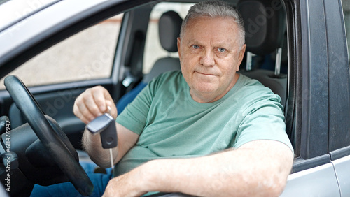 Middle age grey-haired man smiling confident holding key of new car at street