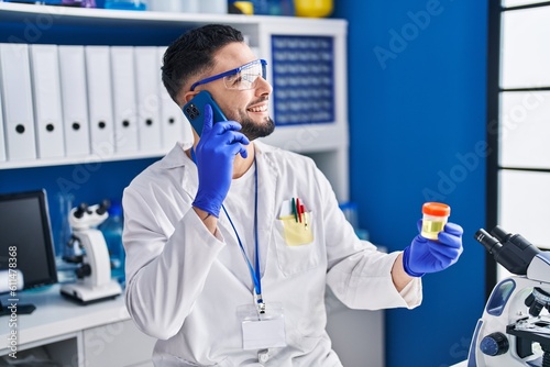 Young arab man scientist talking on the smartphone holding urine test tube analysis at laboratory