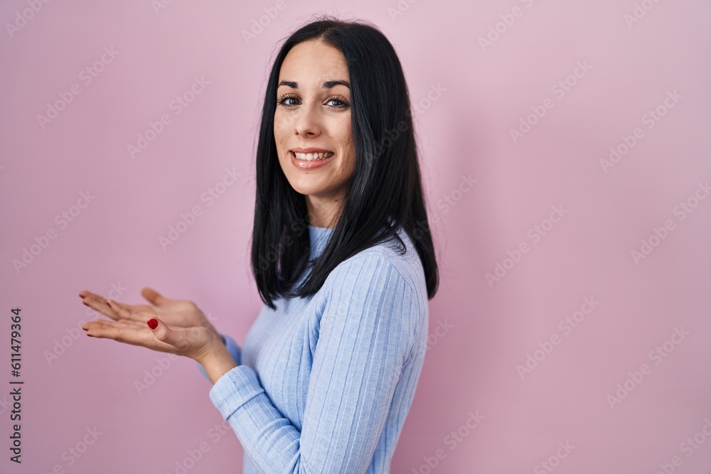 Hispanic woman standing over pink background pointing aside with hands open palms showing copy space, presenting advertisement smiling excited happy Hispanic woman standing over pink background pointing aside with hands open palms showing copy space, presenting advertisement smiling excited happy