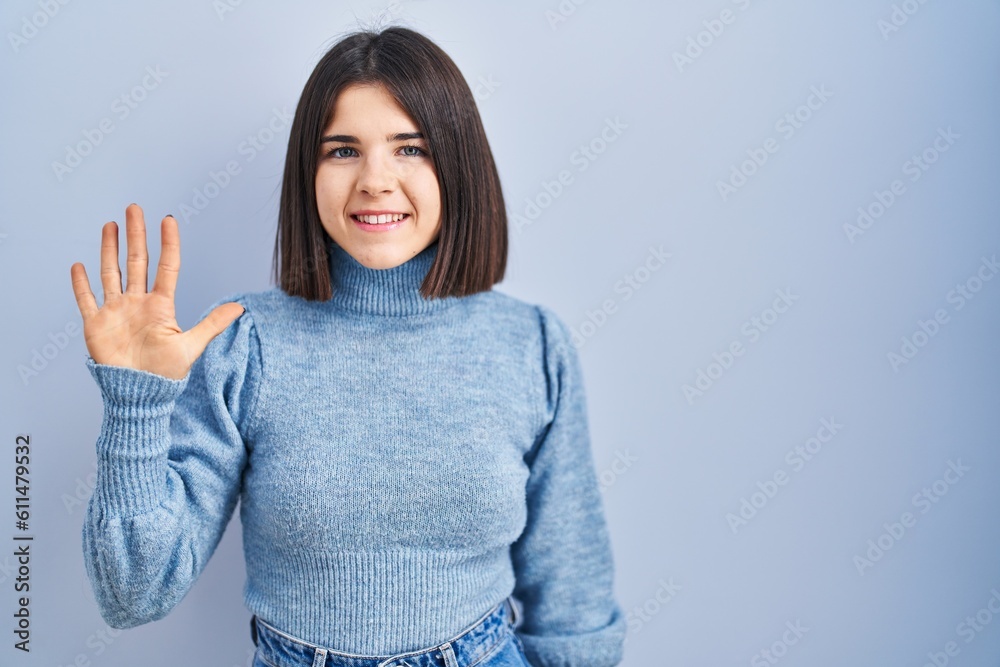 Young hispanic woman standing over blue background showing and pointing up with fingers number five while smiling confident and happy. Young hispanic woman standing over blue background showing and pointing up with fingers number five while smiling confident and happy.