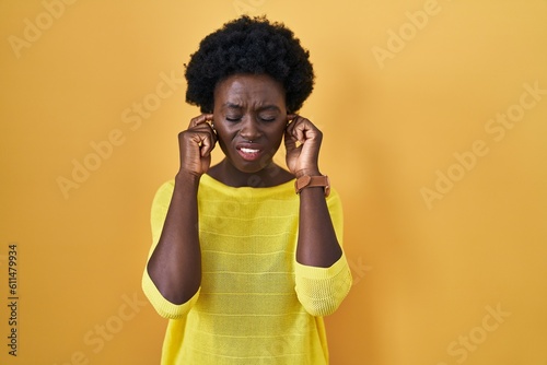 African young woman standing over yellow studio covering ears with fingers with annoyed expression for the noise of loud music. deaf concept. © Krakenimages.com
