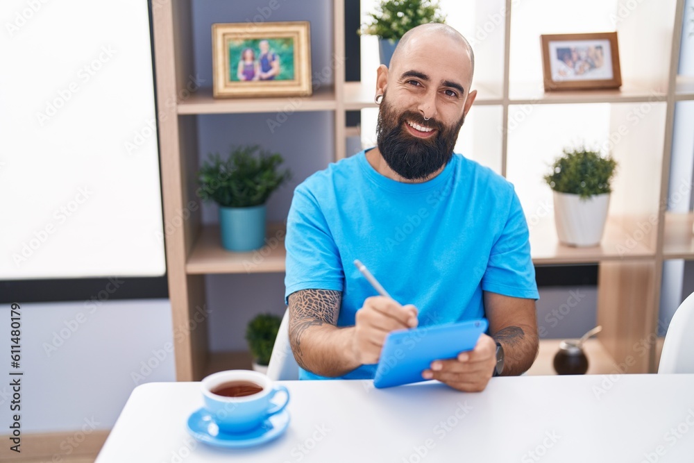 Young bald man using touchpad drinking coffee at home Young bald man using touchpad drinking coffee at home