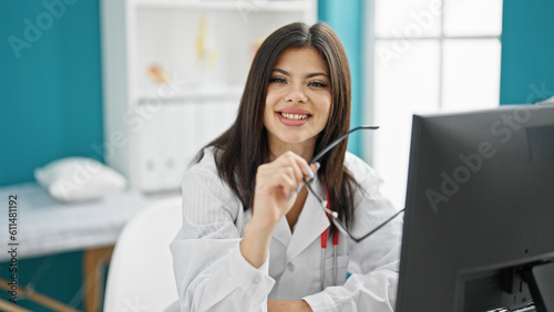Young caucasian woman doctor smiling confident holding glasses at clinic