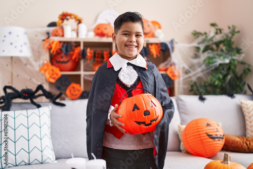 Adorable hispanic boy wearing halloween costume holding pumpkin basket at home