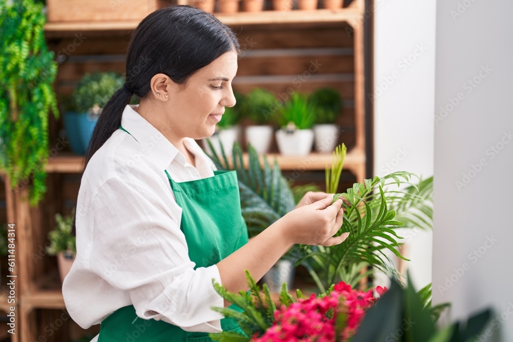 Young beautiful hispanic woman florist smiling confident touching sheet plant at flower shop