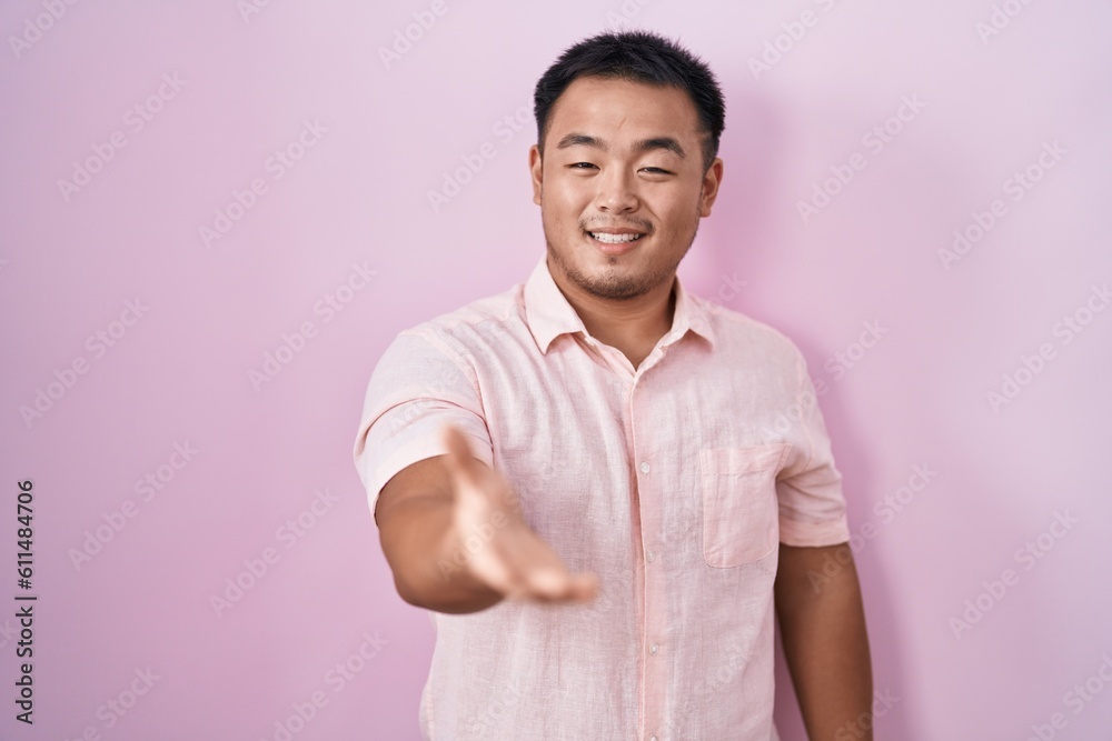 Fototapeta premium Chinese young man standing over pink background smiling cheerful offering palm hand giving assistance and acceptance.