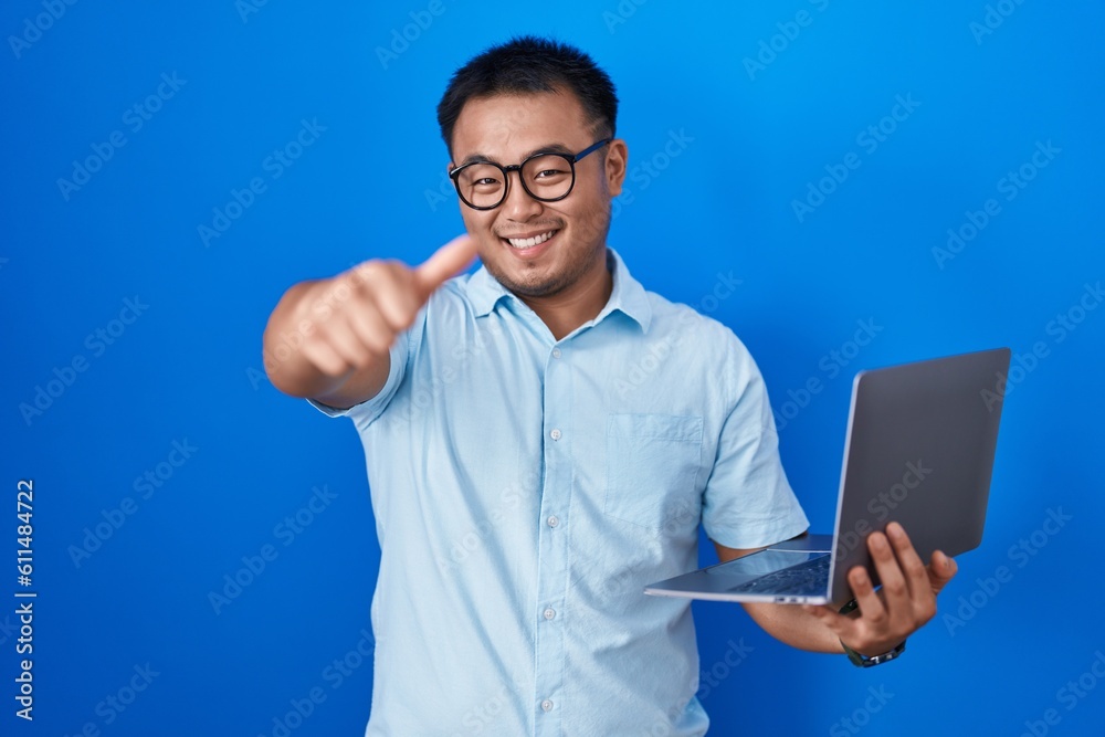 Chinese young man using computer laptop approving doing positive gesture with hand, thumbs up smiling and happy for success. winner gesture. Chinese young man using computer laptop approving doing positive gesture with hand, thumbs up smiling and happy for success. winner gesture.