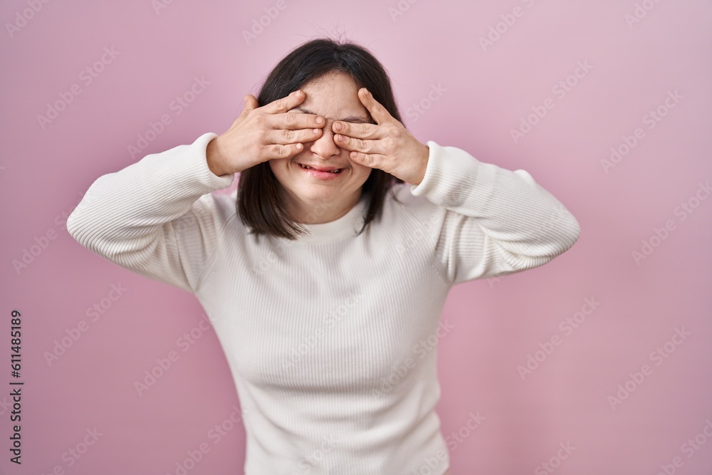 Woman with down syndrome standing over pink background covering eyes with hands smiling cheerful and funny. blind concept. Woman with down syndrome standing over pink background covering eyes with hands smiling cheerful and funny. blind concept.