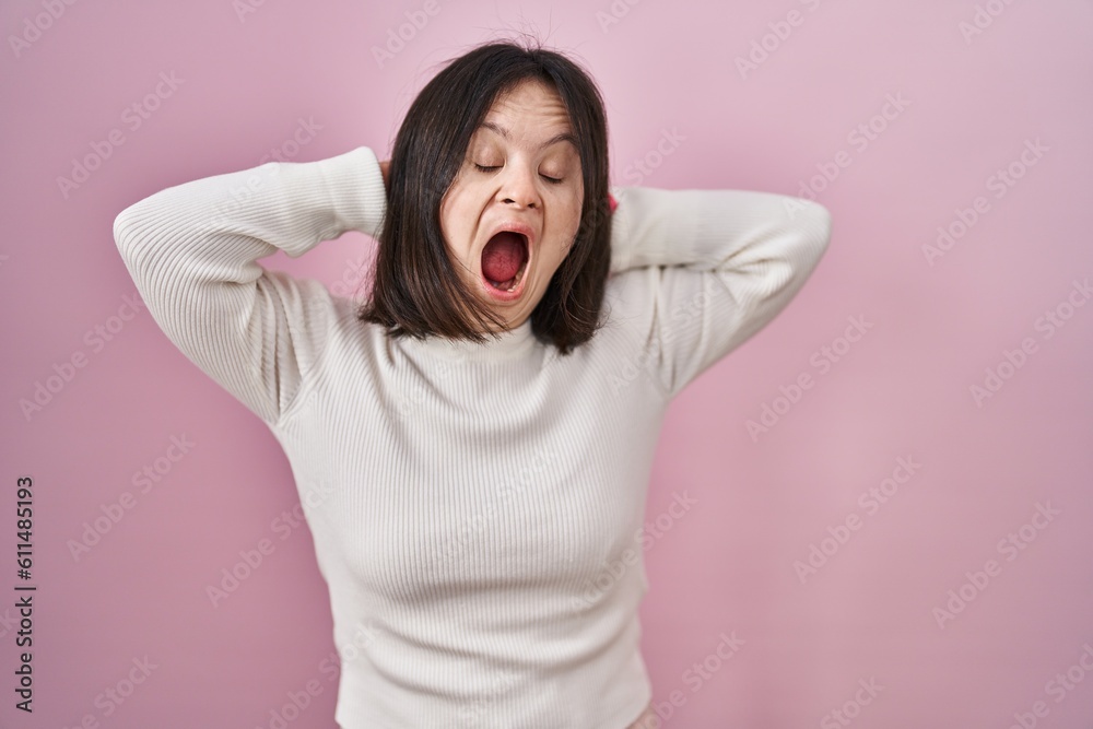 Woman with down syndrome standing over pink background crazy and scared with hands on head, afraid and surprised of shock with open mouth