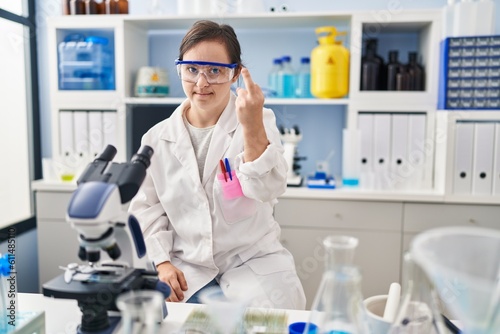 Hispanic girl with down syndrome working at scientist laboratory showing middle finger, impolite and rude fuck off expression