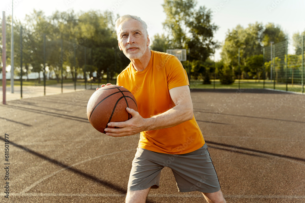 Confident active senior man, retired grandfather in orange t-shirt playing basketball Confident active senior man, retired grandfather in orange t-shirt playing basketball