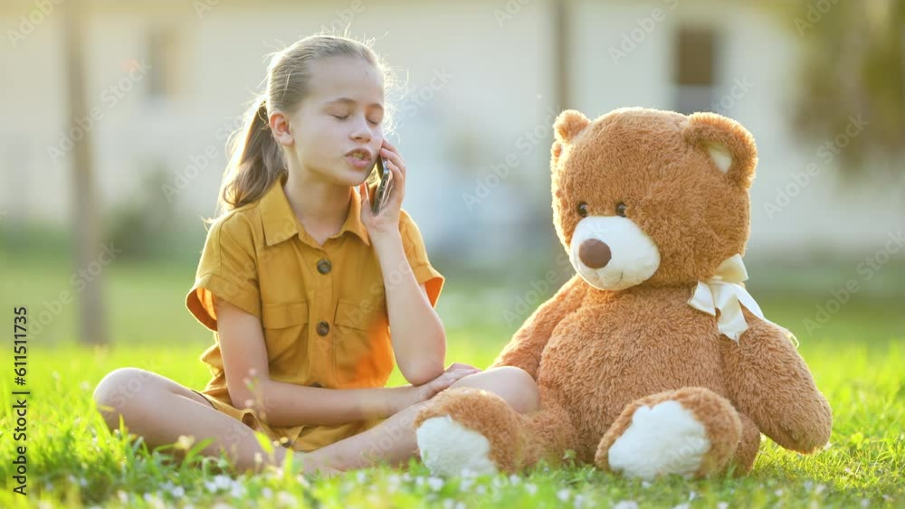 Pretty preteen girl playfully taking with her friend on sell phone sitting outdoors on green grass lawn. Concept of friendship values vídeo do Stock | Adobe Stock 