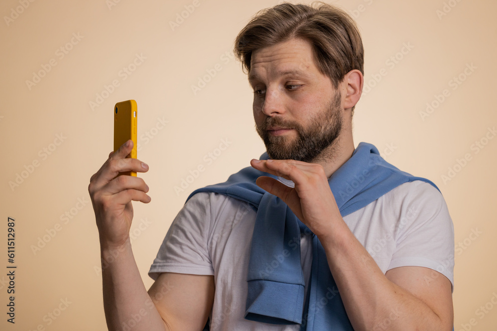 Disinterested young Caucasian man having annoyed boring talk on smartphone. Tired sleepy adult guy talking on mobile phone with friend, making online conversation isolated on studio beige background Disinterested young Caucasian man having annoyed boring talk on smartphone. Tired sleepy adult guy talking on mobile phone with friend, making online conversation isolated on studio beige background