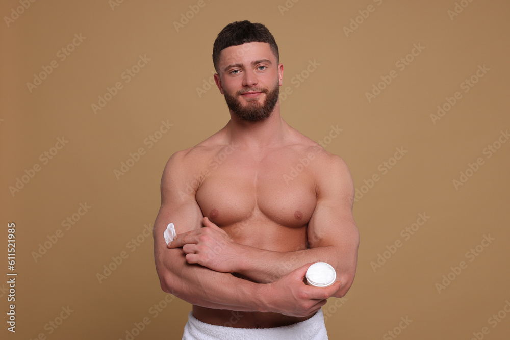 Handsome man applying body cream onto his arm on pale brown background