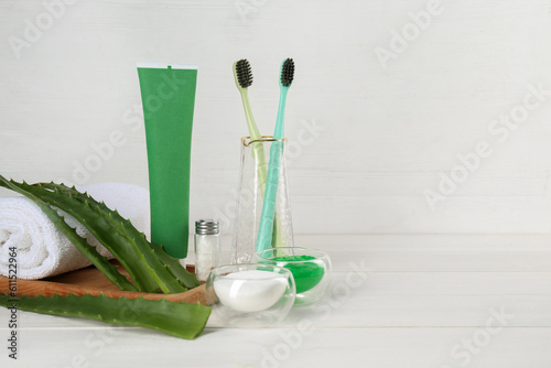 Tube of toothpaste  toothbrushes  fresh aloe vera leaves and care products on white wooden table. Space for text