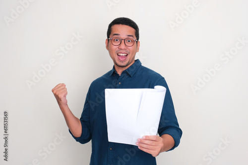 Adult Asian man cheering happily while holding a letter document photo