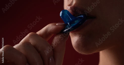 Lick and suck condom. Foreplay before love. Close up woman mouth holding condom. Love, sexuality and safe sex concept. Sensual sex with condom. Choice of safe sex protection. Oral sex with condom.