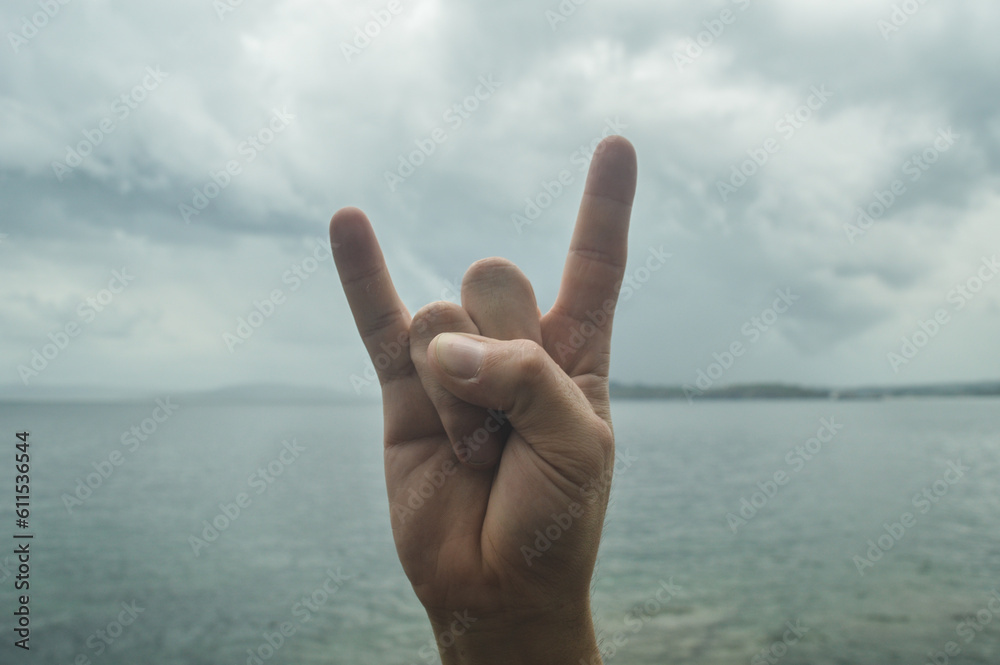 gesturing with the hand, on an outdoor background of sea and sky, rock or horns gesturing with the hand, on an outdoor background of sea and sky, rock or horns