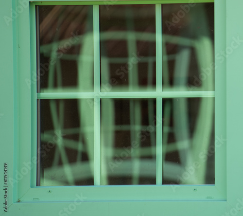 reflection in window of other windows with distortion from glass square window rectangular window panes antique green wooden window frame reflecting more green windows geometrical shapes backdrop 