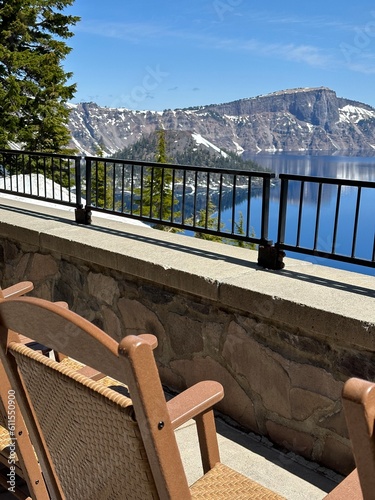 Patio chairs on the terrace of Crater Lake Lodge overlooking the deep blue volcanic lake and rugged snow-dusted cliffs on a sunny day
