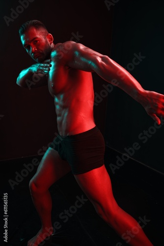 Man bodybuilder posing muscles with nude fitness torso, isolated on black background in neon light. Advertising, sports, active lifestyle, colored light, competition, challenge concept. 