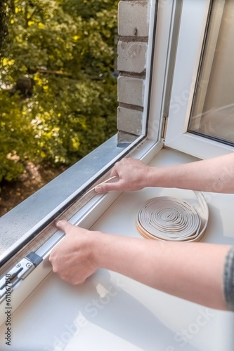 a man puts sealing foam on the window in the room to keep warm. The concept of energy efficiency.