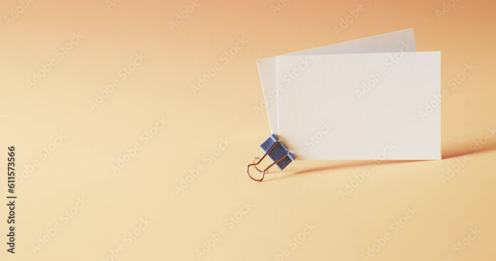 Two blank white business cards with bulldog clip on orange background, copy space, slow motion Two blank white business cards with bulldog clip on orange background, copy space, slow motion