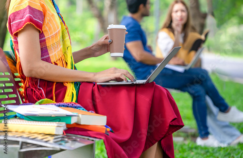 woman transgender in colorful rainbow lgbtq dresses one hand typing laptop,other hand holding a cup of coffee,lgbt people working or studying in the public park,concept of lgbtqi lifestyle,gay pride