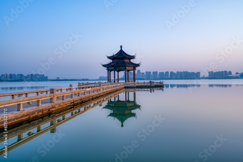 A pavilion and its reflection in the lake. Modern skyscrapers in distance. Photo is taken in Suzhou, Jiangsu province, China. photo