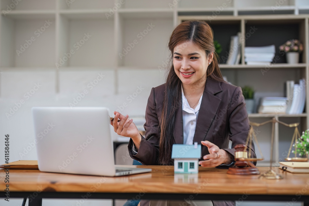 Asian businesswoman lawyer sitting at the office holding a pen taking note working on a loan a sample home mallet a laptop at the table. Asian businesswoman lawyer sitting at the office holding a pen taking note working on a loan a sample home mallet a laptop at the table.