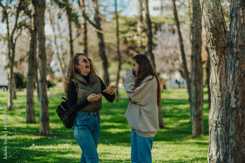 Curly haired girl saw something funny on the phone then she burst out laughing while her brunette friend is having a phone call and looking at her Curly haired girl saw something funny on the phone then she burst out laughing while her brunette friend is having a phone call and looking at her
