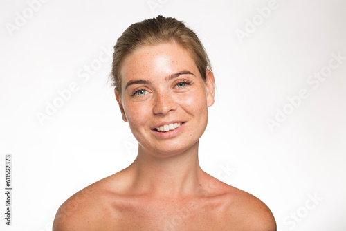 Beautiful girl with freckles look at the camera with her hair tied up in front of the camera on a white background