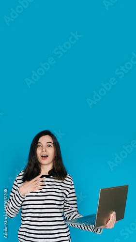 Excited Woman in Striped Sweater Writing Email on Laptop - Modern Technology and Communication Concept. Empty Space for Text - Isolated on Blue Background - Perfect for Business and Technology Themes © Yauhen