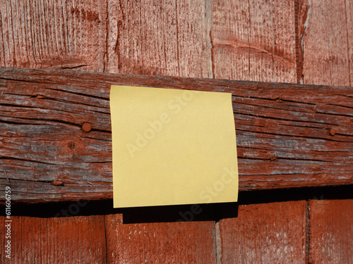 Yellow Blank Sticky Note on Red Weathered Wooden Facade with Great Texture. Blank Area to Copy Your Text. Angled View. Close-Up. photo