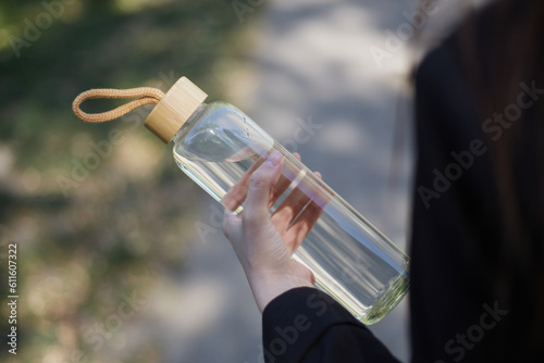Young girl walking with a glass bottle of water in hand. Unrecognizable female person on a walk with a reusable mineral water bottle made of glass