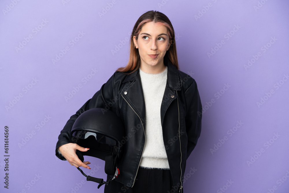 Young caucasian woman holding a motorcycle helmet isolated on purple background and looking up Young caucasian woman holding a motorcycle helmet isolated on purple background and looking up