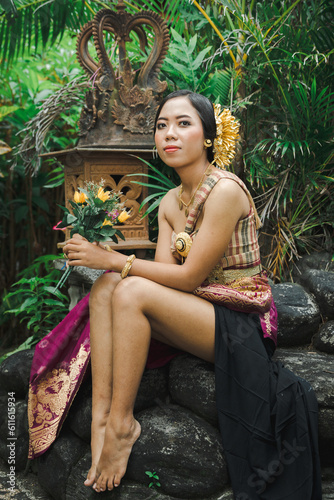 Young woman with bare legs dressed in Balinese costume in the garden