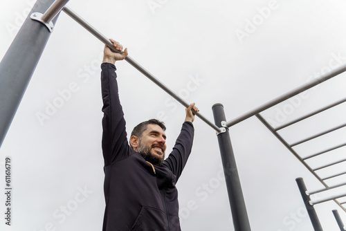 young man dressed in black training on a pull-up bar in an outdoor gym