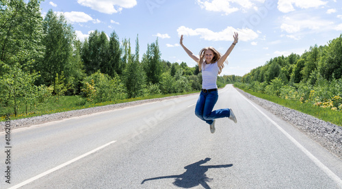 A smiling young girl, a teenager, jumps in the middle of the road in the summer outside the city. The concept of tourism and travel advertising. High quality photo