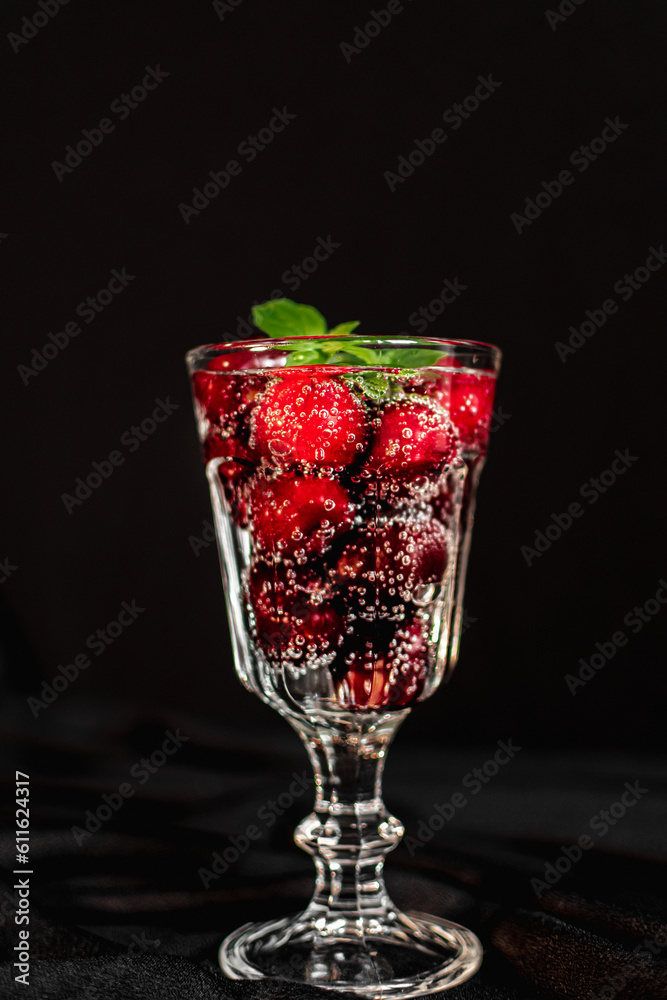 summer cocktail with cherry berries and mint sprigs in a transparent glass on a black background. bubbles in a glass. soft drink summer cocktail with cherry berries and mint sprigs in a transparent glass on a black background. bubbles in a glass. soft drink