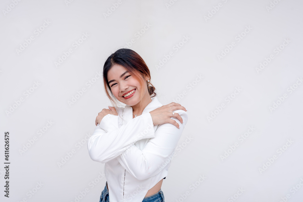A happy and contented young woman looking at the camera with arms crossed to herself in an embrace. Isolated on a white background. A happy and contented young woman looking at the camera with arms crossed to herself in an embrace. Isolated on a white background.