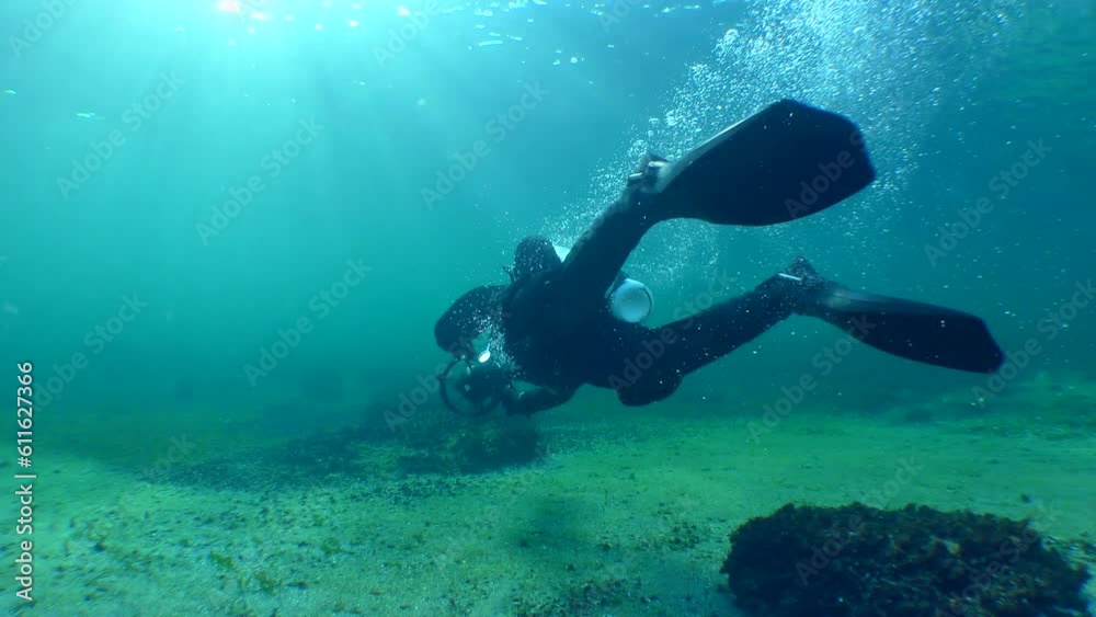 A diver with an underwater scooter makes a U-turn in front of the camera in back sunlight. A diver with an underwater scooter makes a U-turn in front of the camera in back sunlight.