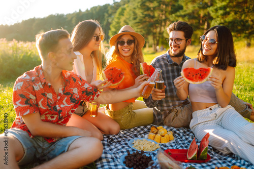 Attractive cheerful people gathering meeting eating watermelon embracing free time on the picnic outdoors. People, lifestyle, travel, nature and vacations concept.