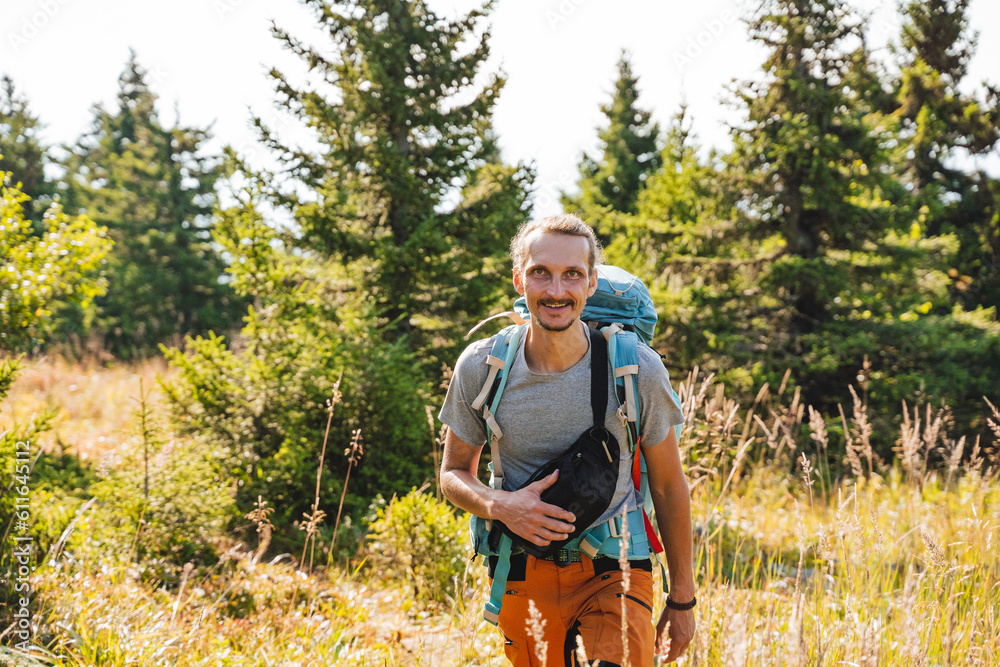 Fototapeta premium A guy cheerfully walks through the forest with a backpack, a tourist route, trekking alone, hiking in the forest, trekking equipment.
